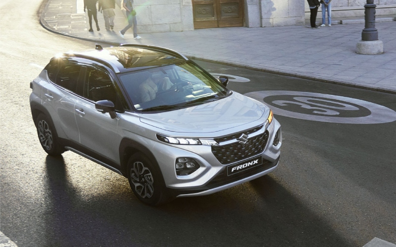 SUV Compacto Suzuki Fronx Híbrido plateado conduciendo por una calle urbana