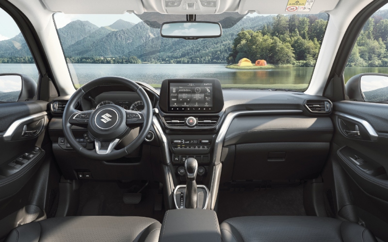 Interior de un Suzuki Grand Vitara, mostrando el volante, la pantalla táctil y asientos de cuero, con un paisaje natural de fondo