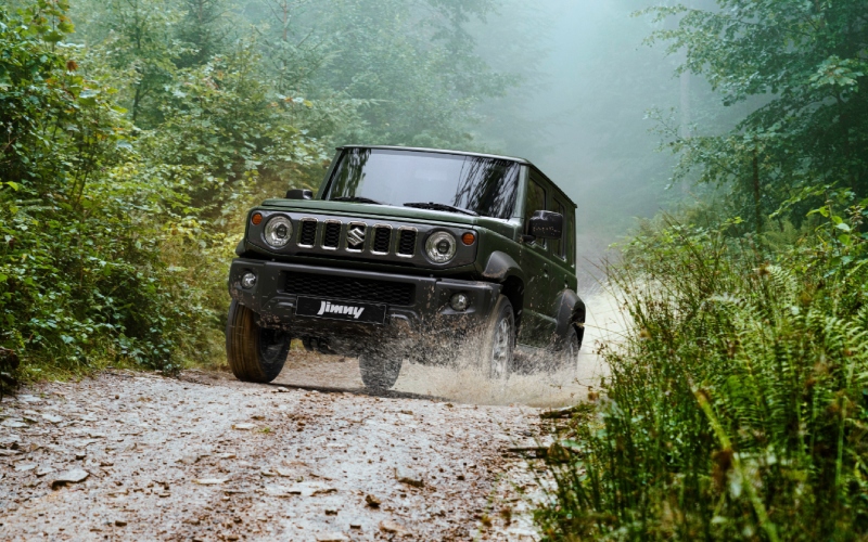 Suzuki Jimny de color verde oscuro circulando por un camino de tierra en un bosque.